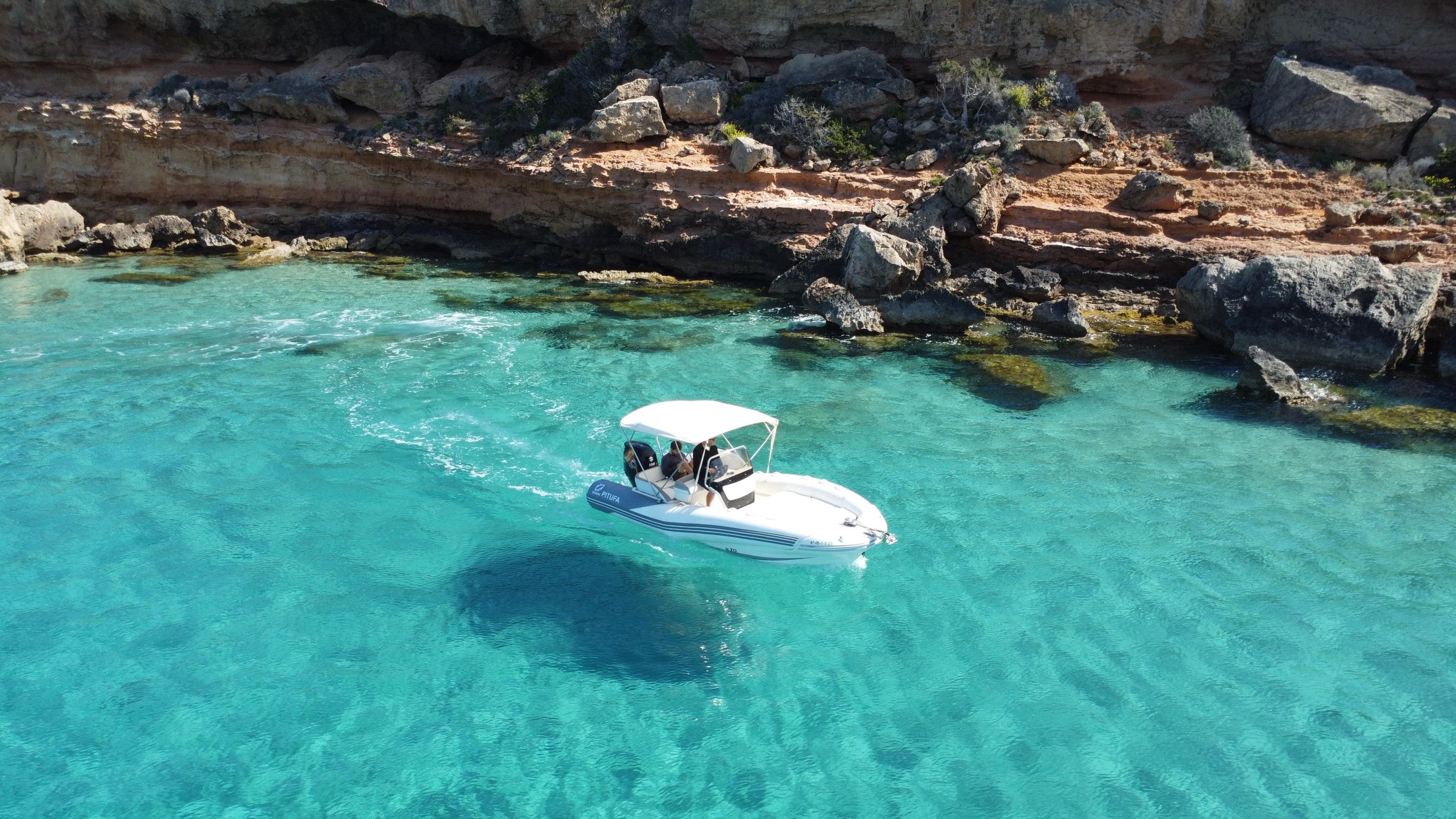 Barco Pitufa navegando junto a los acantilados de una cala en Ibiza